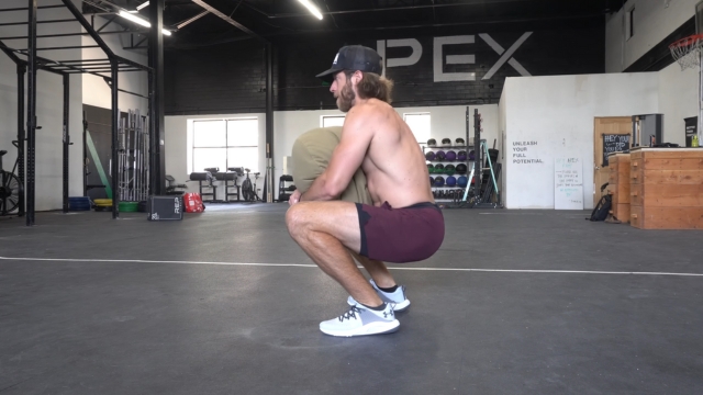Muškarac u čučnju u teretani nosi Under Armour HOVR Rise 3 patike